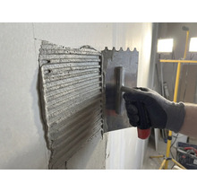 Adezivul pentru gresie este aplicat pe un perete cu o mistrie din oțel inoxidabil