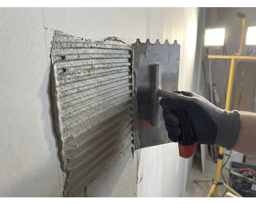 Adezivul pentru gresie este aplicat pe un perete cu o mistrie din oțel inoxidabil