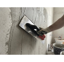 Un meșter aplică tencuială pe un perete cu o gletieră.