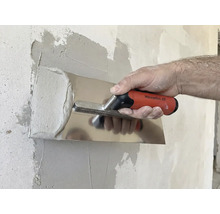 O persoană nivelează gletul cu o gletieră pe un perete.