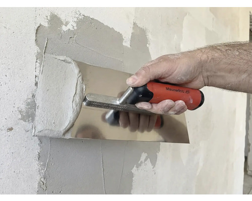 O persoană nivelează gletul cu o gletieră pe un perete.