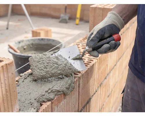 Zidar care aplică mortar și cărămizi pentru construcția unui zid