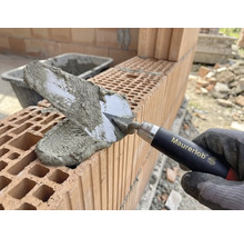 Mână de zidar cu mistrie aplicând mortar pe cărămizi