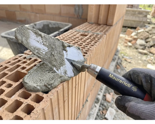 Mână de zidar cu mistrie aplicând mortar pe cărămizi