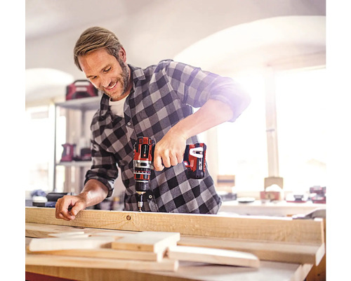 Un bărbat găurește o scândură de lemn cu o șurubelniță electrică cu acumulator.