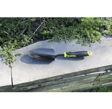 Lopată de grădină pe un zid cu plante în fundal