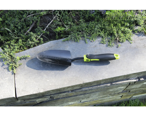 Lopată de grădină pe un zid cu plante în fundal