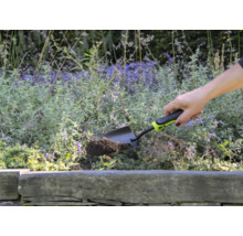 O persoană folosește o lopată mică de grădină pentru a săpa într-un strat de flori.