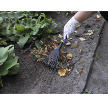 O persoană adună frunzele cu o greblă de frunze în grădină.