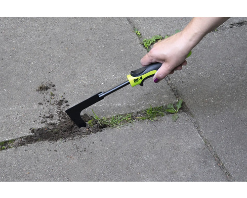 O mână folosește o racletă pentru rosturi pentru a îndepărta buruienile dintre pietrele de pavaj.