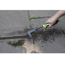 O persoană îndepărtează buruienile cu o racletă de rosturi pe o suprafață pavată.