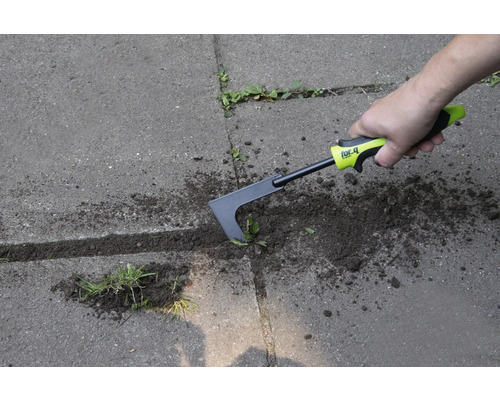 O persoană îndepărtează buruienile cu o racletă de rosturi pe o suprafață pavată.