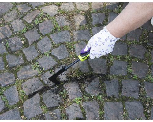 O persoană îndepărtează buruienile cu o racletă de rosturi de pe o potecă pavată.