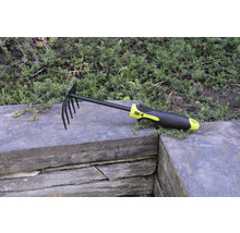 Greblă de frunze și greblă de grădină cu dinți și mâner din plastic pe zid de piatră