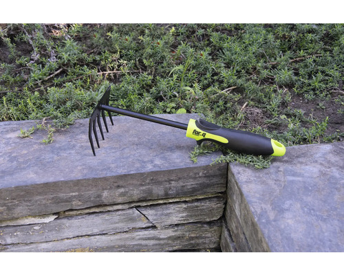 Greblă de frunze și greblă de grădină cu dinți și mâner din plastic pe zid de piatră