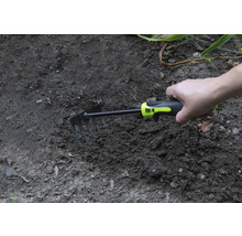 O mână ține o sapă mică în pământul din grădină