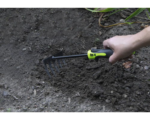 O mână ține o sapă mică în pământul din grădină