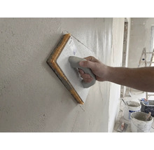 Mână care utilizează o driscă cu burete pentru finisarea tencuielii de pe perete.