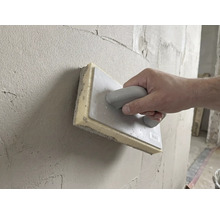 Mână care folosește un drisc cu burete de 28 pe 14 centimetri pentru a netezi tencuiala proaspătă pe un perete.