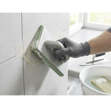 O persoană care chituiește plăci de faianță cu o gletieră pentru rosturi. În fundal se află o găleată cu apă, un burete și o mistrie.