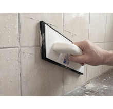 Persoană care chituiește rosturile faianței cu o drișcă de rostuit din plastic și cauciuc spongios.