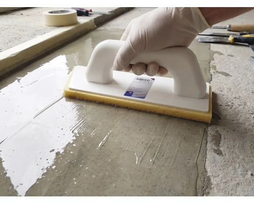 O persoană folosește o driscă cu burete, cu mâner alb și burete galben, pe o suprafață de ciment umedă.