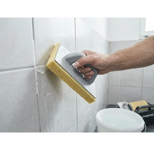 O persoană curăță plăci de faianță proaspăt chituite cu o drișcă cu burete și apă.