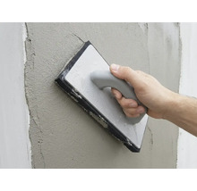 O mână netezește tencuiala proaspătă de pe un perete cu o driscă cu burete.