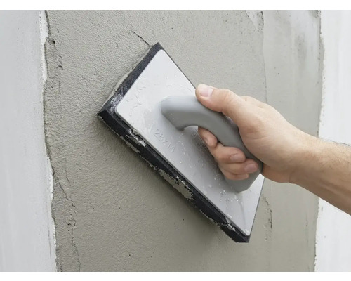 O mână netezește tencuiala proaspătă de pe un perete cu o driscă cu burete.