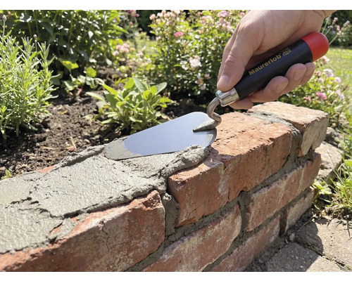 Mână cu mistrie Maurerlob aplicând mortar pe un zid de cărămidă în grădină.