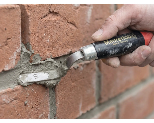 O persoană folosește o mistrie pentru rostuit Maurerlob pentru a aplica mortar între cărămizi roșii.