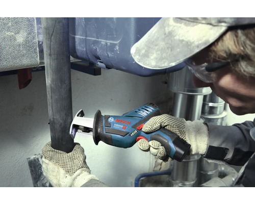 Meșter care taie o țeavă închisă la culoare cu un fierăstrău tip sabie cu acumulator Bosch Professional într-o zonă de lucru cu țevi metalice argintii.