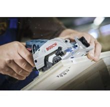 O persoană taie o placă de lemn cu un ferăstrău circular Bosch, fiind vizibile așchii de lemn.