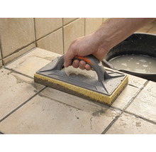 Drișcă cu buret folosită pentru curățarea plăcilor de faianță proaspăt chituite. O mână ghidează drișca pe plăcile ude.