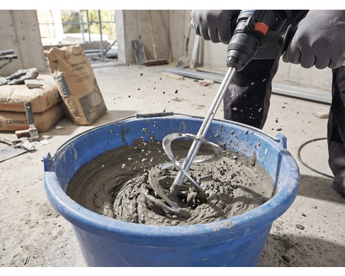 O persoană amestecă mortar cu un agitator și un malaxor într-o găleată albastră pe un șantier.