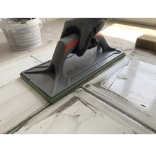 Mână cu mănușă de protecție folosind o drișcă pentru rostuirea plăcilor de gresie.