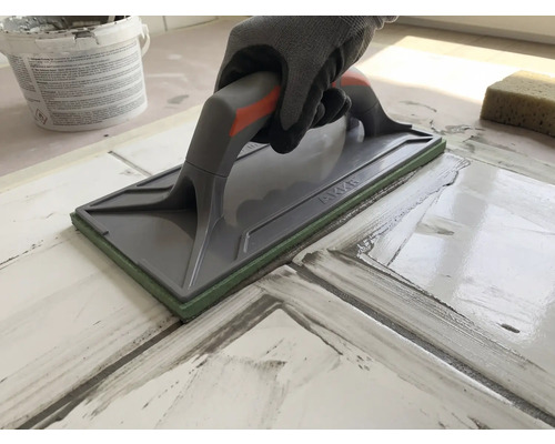 Mână cu mănușă de protecție folosind o drișcă pentru rostuirea plăcilor de gresie.