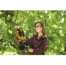 Femeie care utilizează un ferăstrău sabie cu acumulator Worx pentru toaletarea unui copac în grădină. Poartă ochelari și mănuși.