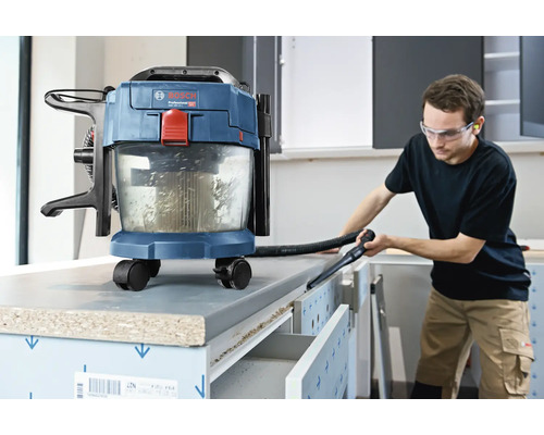 Aspirator cu acumulator Bosch pentru aspirare umedă și uscată, utilizat pentru curățarea unui banc de lucru într-un atelier luminos.