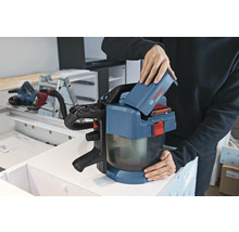 O persoană introduce un acumulator de 18 Volți într-un aspirator cu acumulator Bosch Professional GAS 18 Volt-1 într-un atelier.