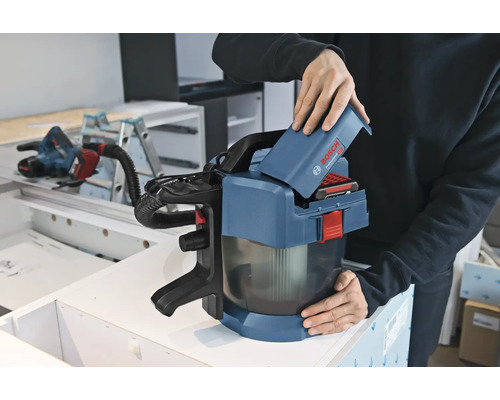 O persoană introduce un acumulator de 18 Volți într-un aspirator cu acumulator Bosch Professional GAS 18 Volt-1 într-un atelier.