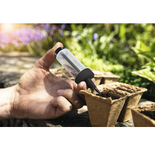 O mână folosește un semănător pentru semănarea semințelor în ghivece de cultură biodegradabile într-o grădină luminoasă.