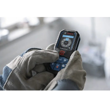 Telemetru cu laser Bosch Professional operat de mâini în mănuși de lucru, afișaj digital cu funcții de măsurare.