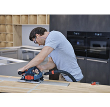 Bărbat care utilizează un ferăstrău circular cu șină de ghidare și aspirare a prafului pe un blat de lemn într-o bucătărie.