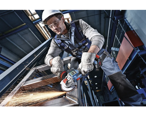 Meșter în echipament de protecție care prelucrează o structură de oțel cu un polizor unghiular cu acumulator sub formă de scântei.