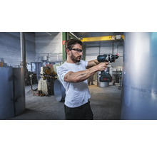 Meșter cu ochelari de protecție care utilizează o mașină de găurit cu acumulator Bosch ProCore 18 Volt pe o țeavă de metal într-un atelier industrial.