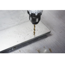Burghiu pentru metal care găurește o placă metalică plată cu așchii de metal pe suprafață.