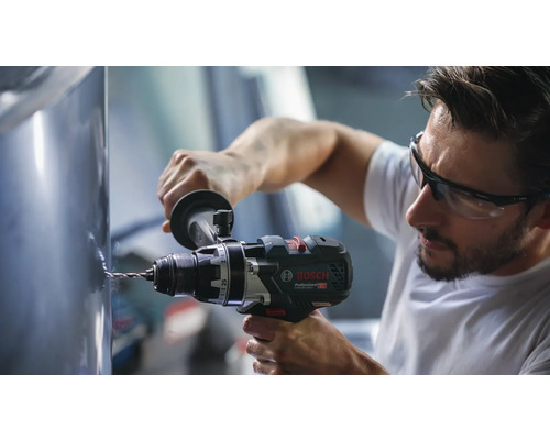 Meșterul găurește o suprafață metalică cu o mașină de găurit și înșurubat cu acumulator Bosch Professional. Acesta poartă ochelari de protecție.