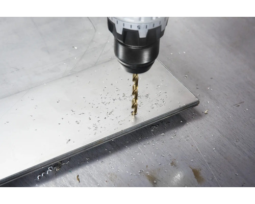 Burghiu pentru metal care găurește o placă metalică plată cu așchii de metal pe suprafață.