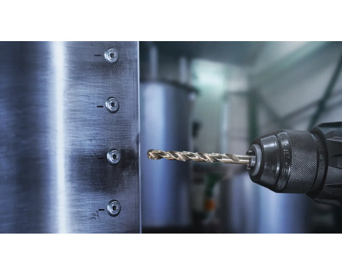 Burghiu pentru metal într-o mandrină în fața unei plăci metalice periate cu orificii.